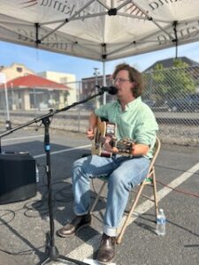 man with curly hair playing the guitar and singing in a tent